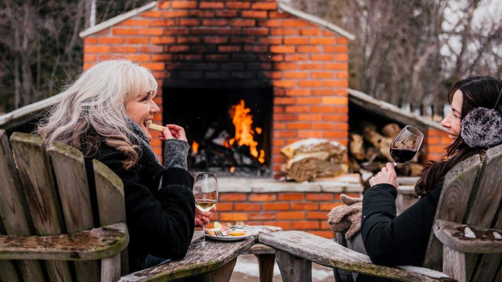 Two women enjoying wine by the fire